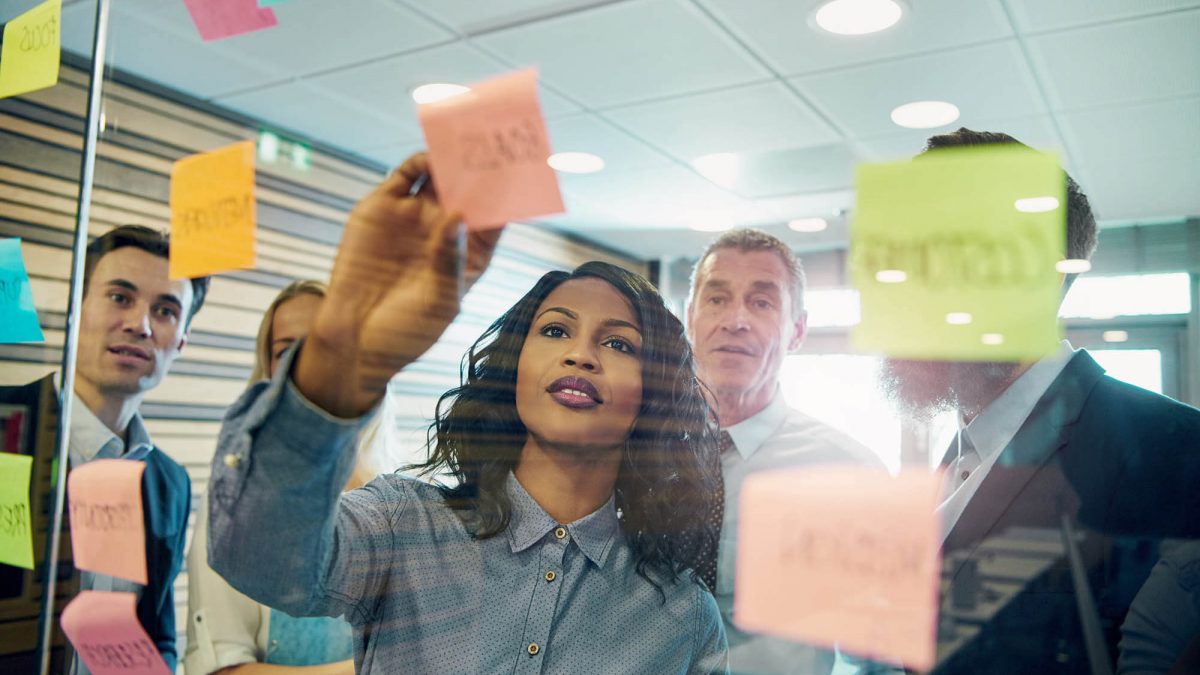 Grupo de pessoas em reunião discutem ideias utilizando cartões e post-it