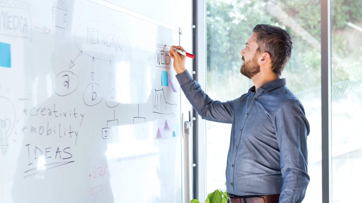 Homem desenhando organograma com metas em whiteboard